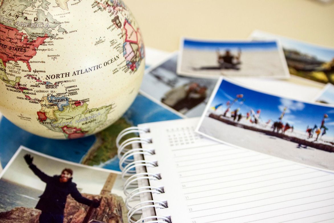 Imagem de uma mesa com cadernos, fotos de viagens e um globo terreste